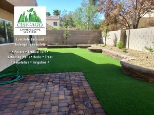 This complete backyard transformation by Chicago Landscape of Las Vegas showcases a seamless integration of functional hardscaping and water-smart greenery. The design features a large interlocking paver patio and a matching side walkway that transitions into a lush, synthetic turf lawn and elevated stone planter beds. The final result is a multi-textured outdoor oasis that combines professional masonry with low-maintenance desert landscaping and modern irrigation.
