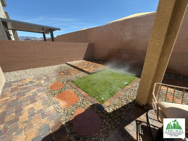 Decorative paver patio, small natural grass area with sprinklers, and raised paver platform in a Las Vegas backyard.