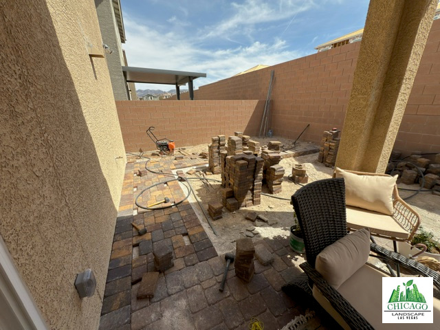 Partially installed backyard pavers with stacked materials beside the covered patio.