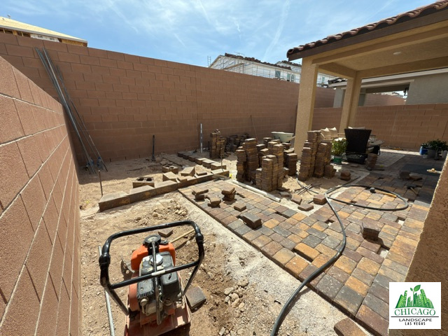 Backyard paver construction with raised edging, stacked pavers, and a plate compactor.