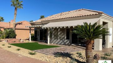 Completed backyard paver patio and synthetic turf bordered by decorative rock.