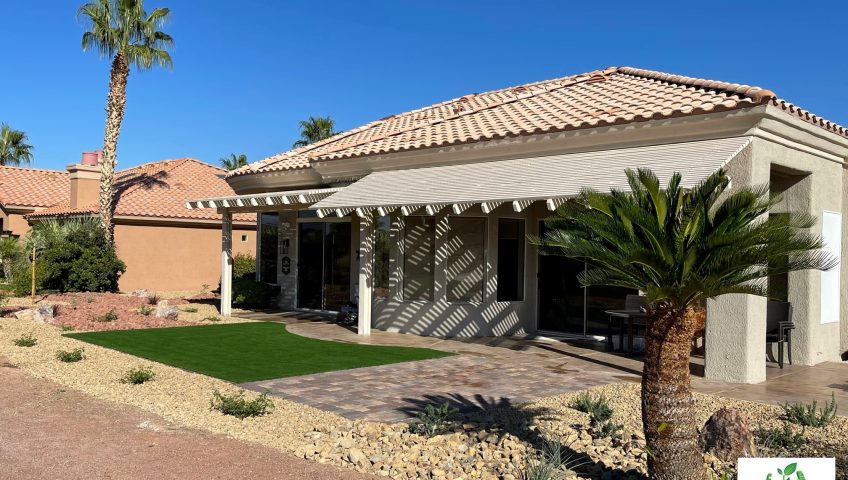Completed backyard paver patio and synthetic turf bordered by decorative rock.