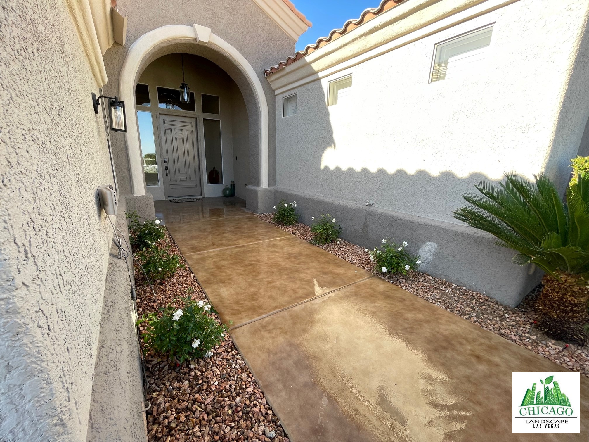 Flowering plants and decorative rock border the walkway to the front door.