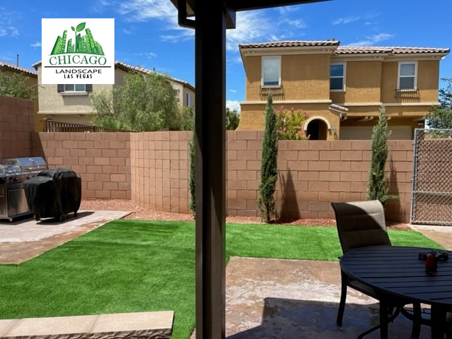 Artificial turf beside the covered patio, with Italian Cypress trees in a decorative rock border along the wall.