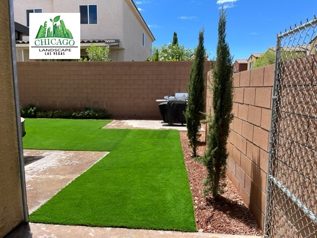 Italian Cypress trees line a reddish landscape rock border beside artificial turf and a side gate.